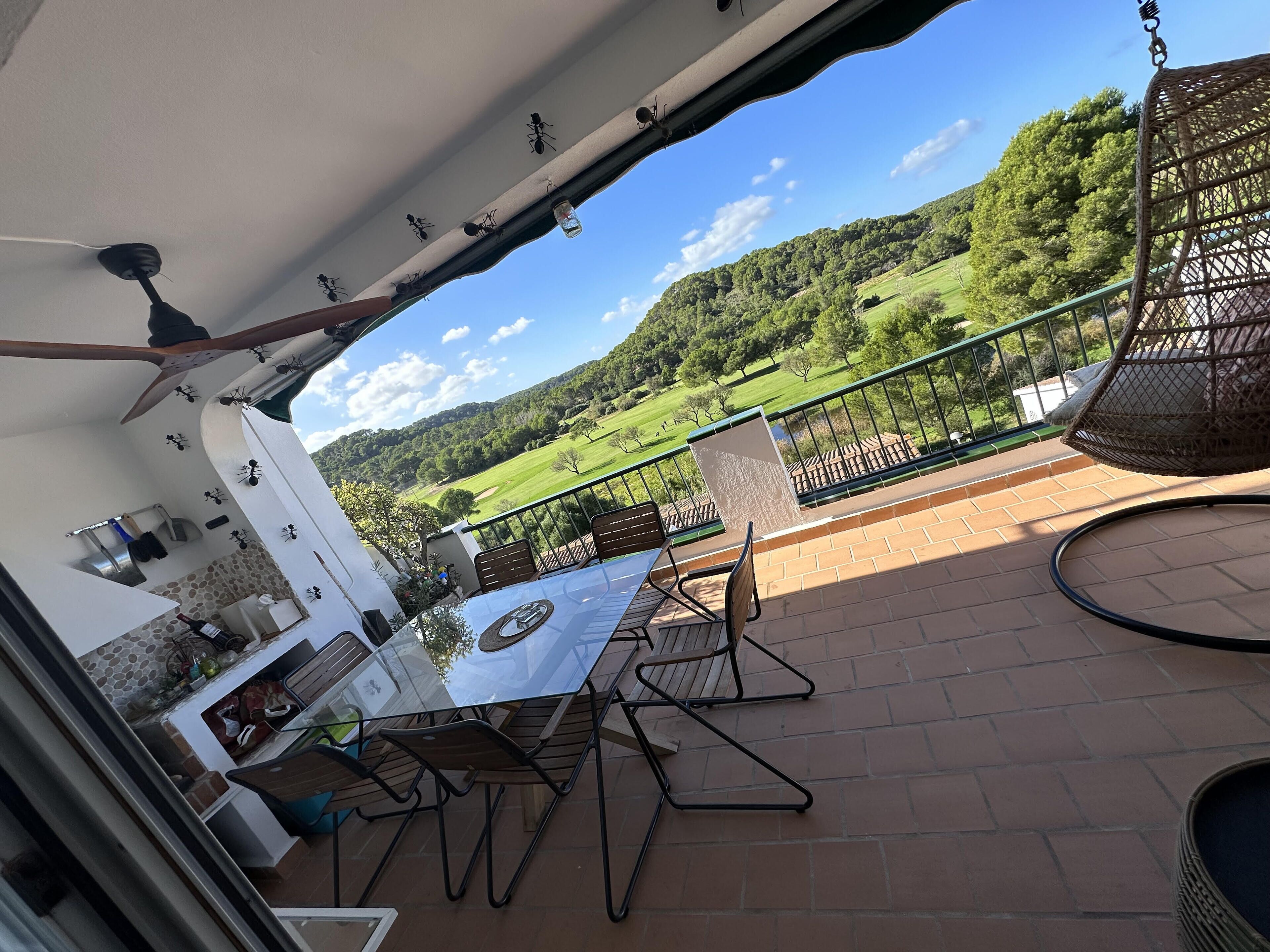 A patio with a table and chairs, a hanging chair, and a view of a green landscape.
