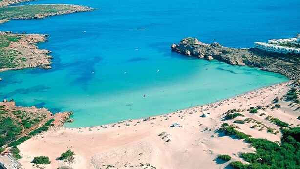 An aerial view of a coastal area with a sandy beach, clear turquoise waters, rocky outcrops, and a resort with multiple buildings. - Flat Surrounded by Nature, With Pool, and Beach Nearby (Son Parc)
