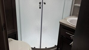 A bathroom with a glass shower enclosure, a toilet, and a sink. - Barbara's little camper! (Sevierville)