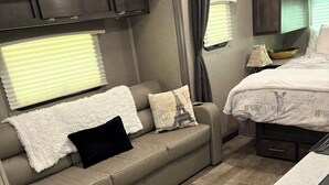 A compact RV interior with a kitchenette, a sofa with decorative pillows, and a bed with a Paris-themed bedspread. - Barbara's little camper! (Sevierville)