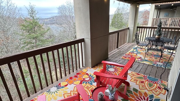 A covered outdoor area with a wooden deck, colorful patterned rugs, and red chairs.