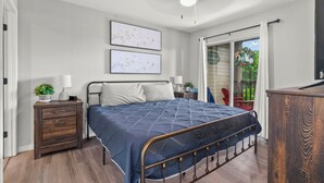 A bedroom with a bed, nightstands, a dresser, and a sliding glass door leading to a balcony.