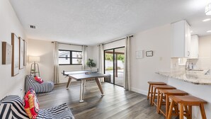 Ein modernes Wohnzimmer mit einem Tischtennisch, gestreiften Sitzsäcken und einer Küchenzeile mit Barhocker.