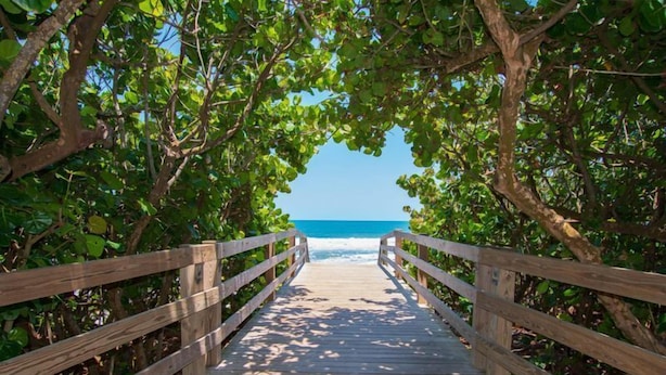 A wooden boardwalk leading to a beach with clear blue water.