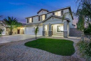 A two-story house with a garage, a well-maintained lawn, and a driveway. - Park Heaven: Pool, Spa, Fire Pit, Games, BBQ! (Coachella)