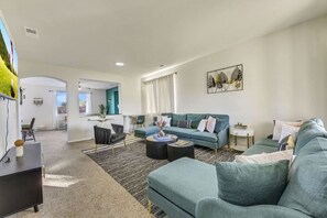 A modern living room with a teal sofa, a coffee table, and a black armchair. There is a painting on the wall and a window with curtains. - Park Heaven: Pool, Spa, Fire Pit, Games, BBQ! (Coachella)