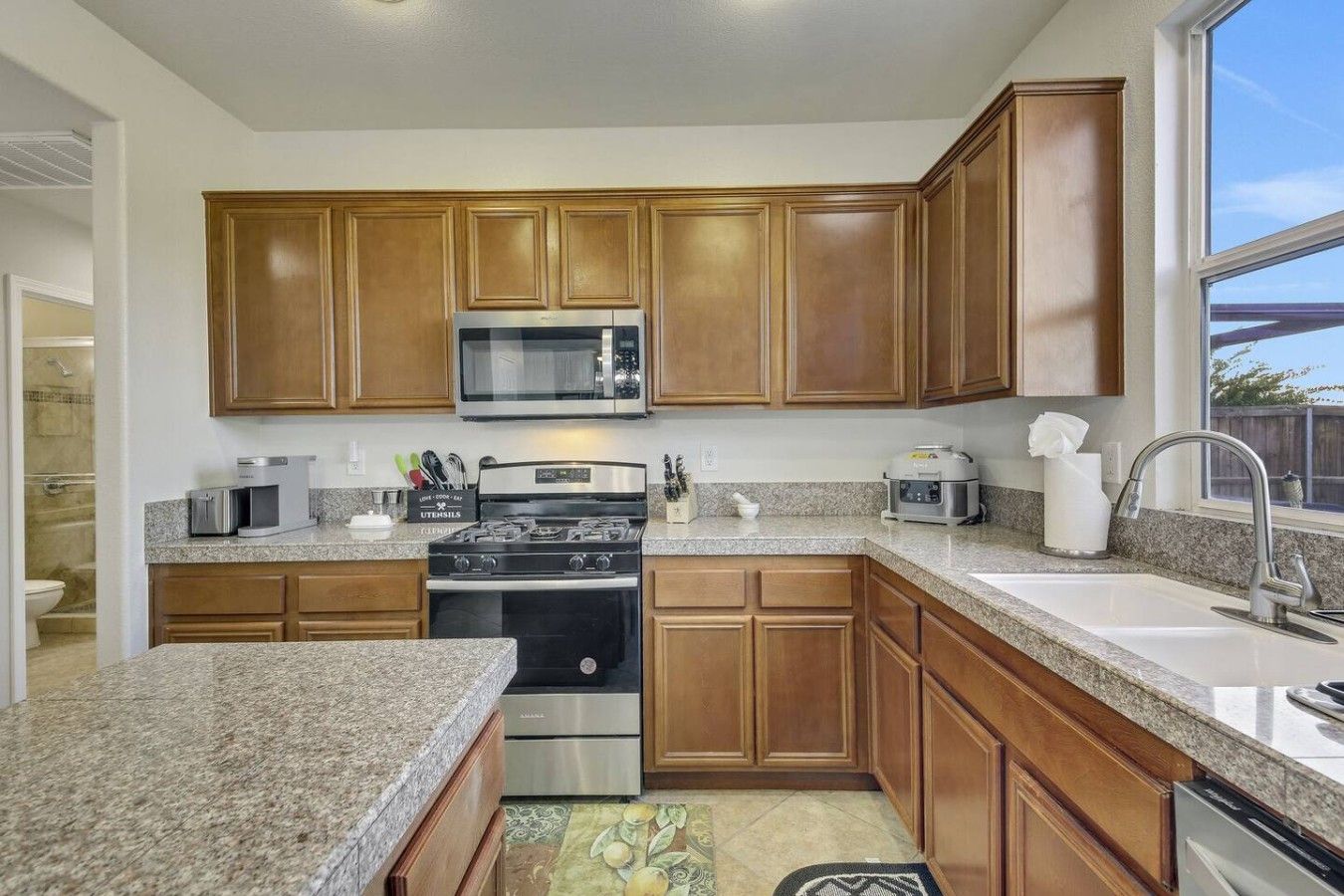 A kitchen with wooden cabinets, stainless steel appliances, granite countertops, and a window providing natural light.