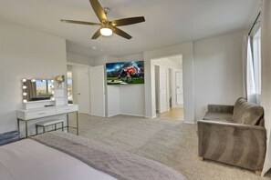 A bedroom with a bed, a vanity with lights, a ceiling fan, a TV, and a sofa.