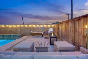 An outdoor patio with a pool, lounge chairs, a grill, and string lights.