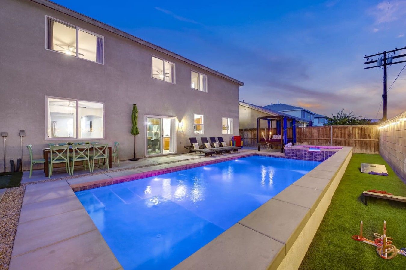 A residential backyard with a swimming pool, a covered patio, and a fenced area with outdoor furniture.