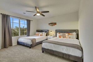 A hotel room with two beds, a ceiling fan, a window with curtains, and a view of palm trees.