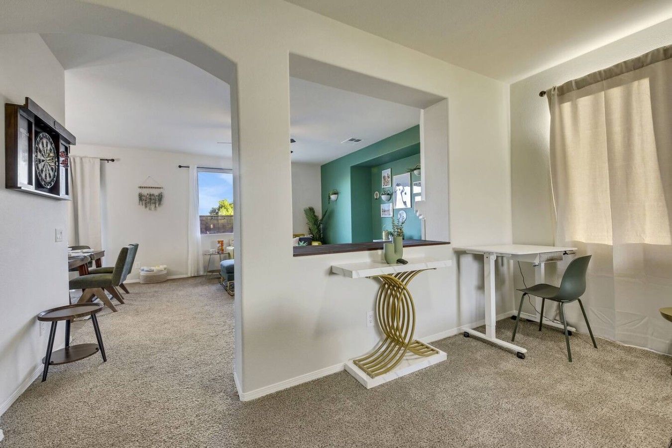 A modern living room with a dining area, a kitchen visible through an archway, and a white desk with a chair.
