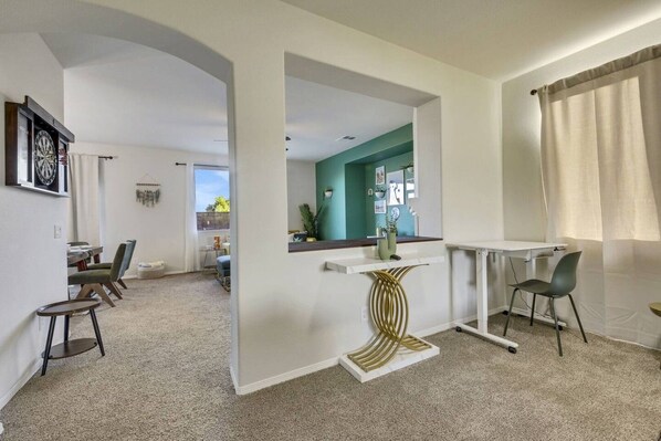 A modern living room with a dining area, a kitchen visible through an archway, and a white desk with a chair.