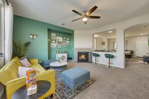 A living room with a yellow sofa, blue armchair, and ottoman, a fireplace, and a ceiling fan.