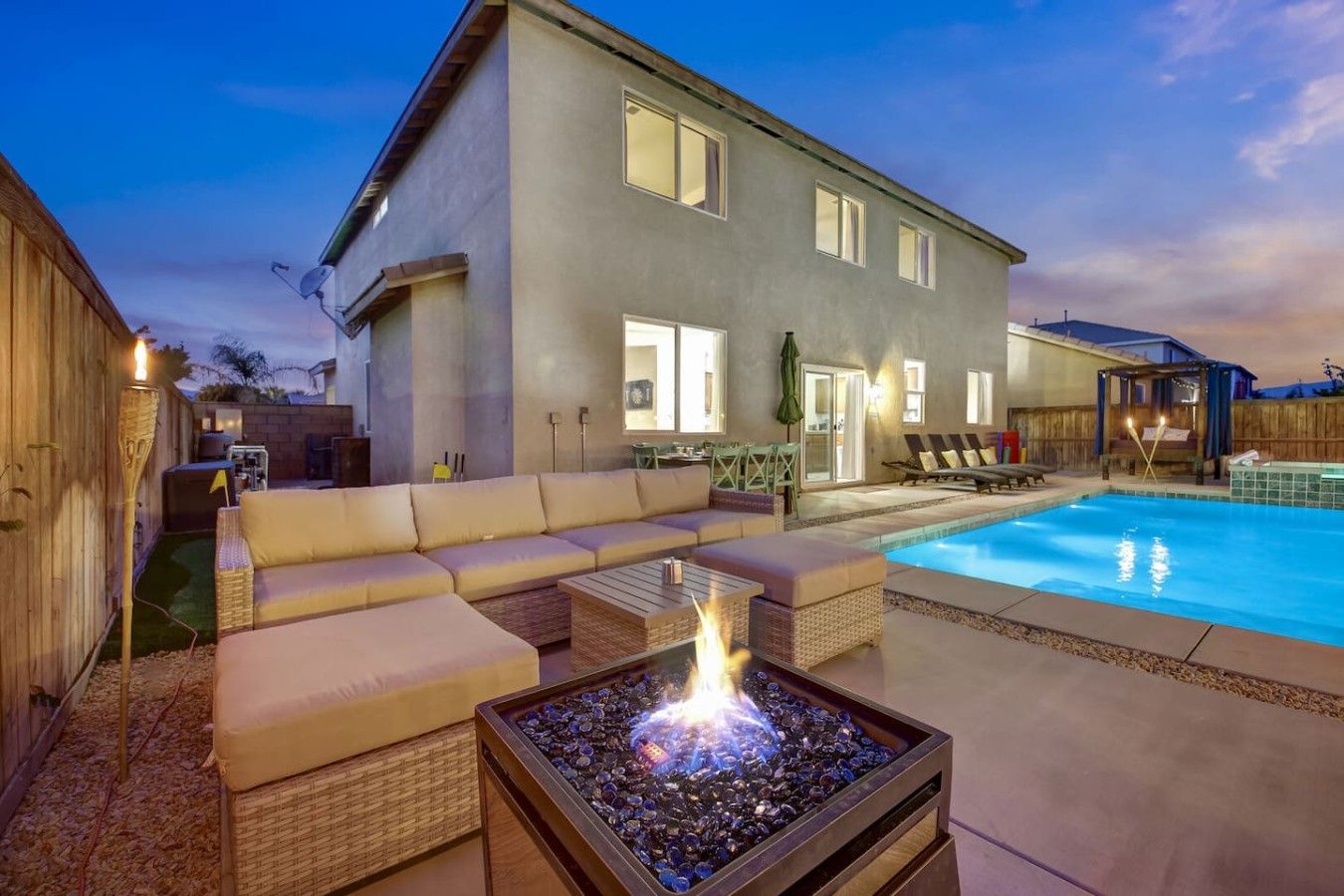 A backyard with a swimming pool, a covered patio area, and a fire pit.