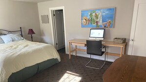 A hotel room with a bed, a desk with a computer, a chair, and a wooden table.