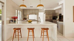 Una cocina moderna con una isla grande, taburetes de madera e iluminación colgante.