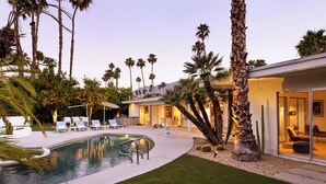 Una casa moderna con piscina, palmeras y mobiliario de exterior.