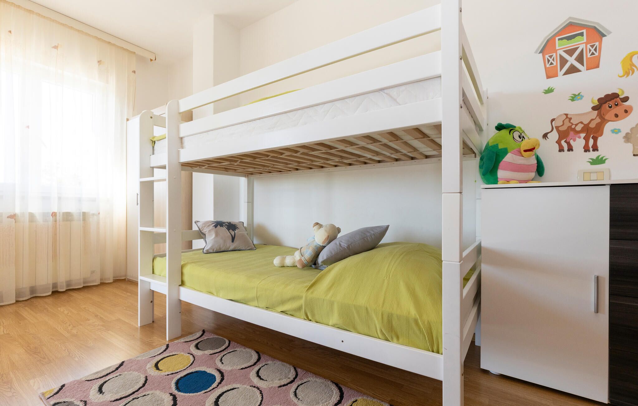 A bunk bed room with a green bedspread, a teddy bear, and a refrigerator with farm-themed stickers.