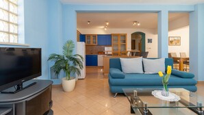 Een woonkamer met een flatscreen televisie, een blauwe bank, een salontafel en een potplant.