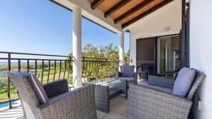 Een balkon met rieten meubilair, een glazen tafel en uitzicht op het landschap.