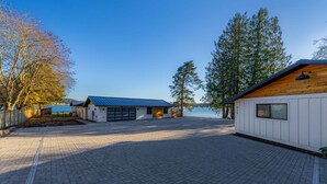 A waterfront property with a paved driveway leading to a building with a blue roof, a wooden deck, and a view of the water.