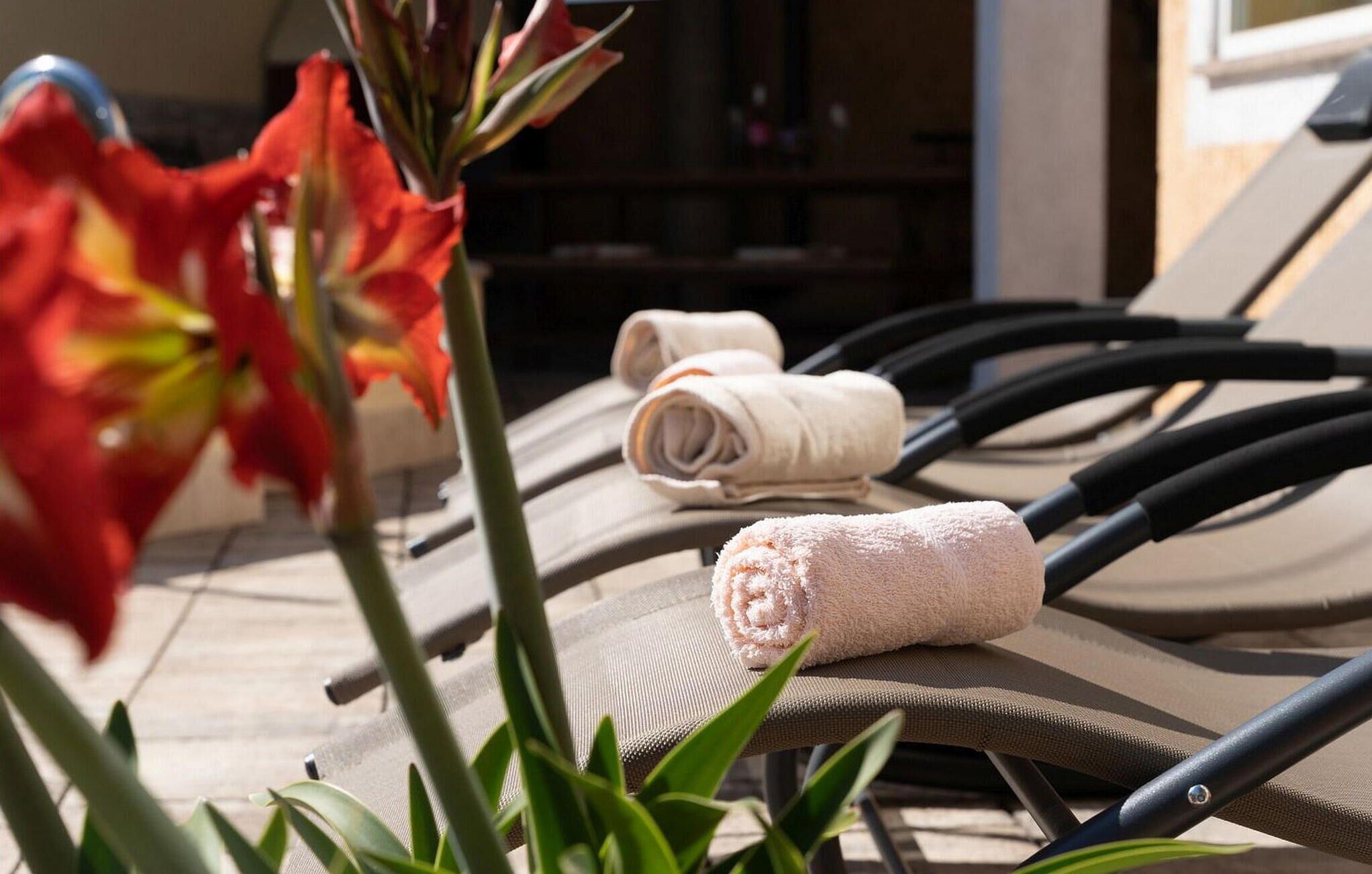 A sun lounger with rolled towels and a red flower in the foreground.