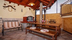Un área de comedor al aire libre de estilo rústico, con un banco de madera, una mesa y un muro de piedra.
