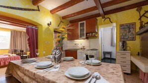 Un comedor con una mesa preparada para cuatro personas, una cocina al fondo y una ventana con cortinas.