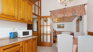 Una cocina con armarios de madera, un microondas y una tetera. Hay una zona de comedor con una mesa y sillas.