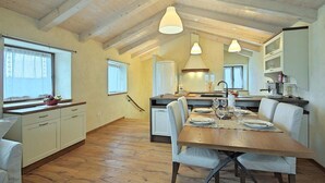 Eine geräumige Küche mit Holzbalken, eine Essecke mit Holztisch und -stühlen sowie ein Blick in den angrenzenden Wohnbereich.
