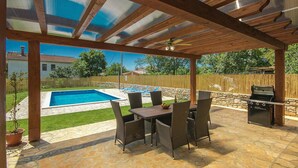 Eine überdachte Terrasse mit Pool, Gartenmöbeln und Grill.
