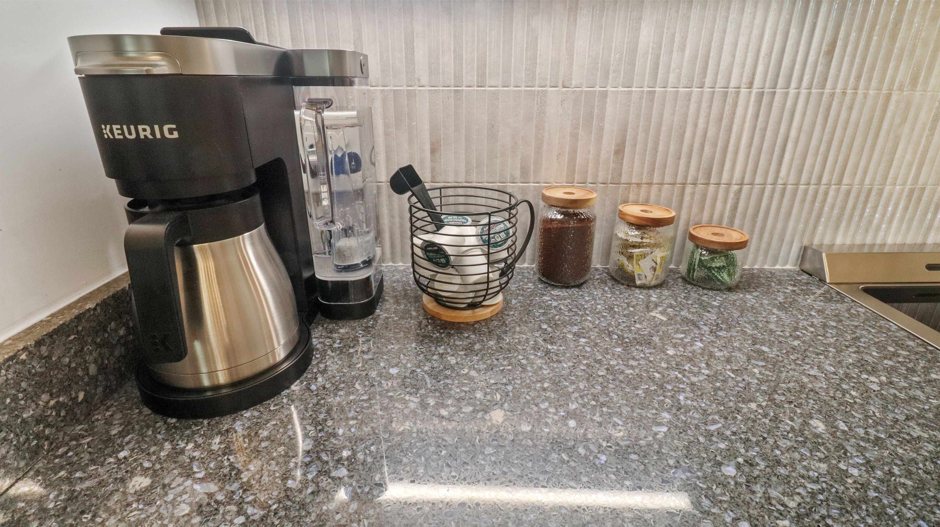 Una cocina con una cafetera Keurig, una licuadora, un molinillo de café y tres frascos con tapa.