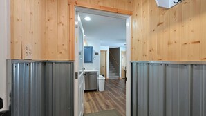 A hallway with wooden walls and a metal door, leading to a kitchen area with a white trash bin and a staircase in the background. - Osprey Point - Lakefront Dock, Kayaks & Fire Pit (Cable)