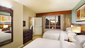 A hotel room with two beds, a dresser, a desk, and a window with a city view. - Waikiki | Waikiki Lagoon Escape | Pool & Beach | 2BR (Honolulu)
