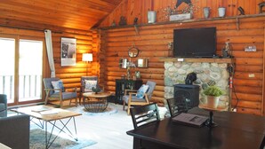 L’intérieur chaleureux d’un chalet avec une cheminée en pierre, des murs en bois et un téléviseur fixé au-dessus.