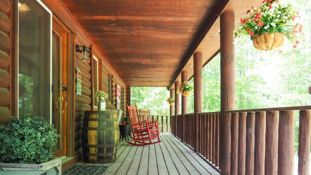 Une véranda en bois avec une balustrade, une chaise berçante et un tonneau.