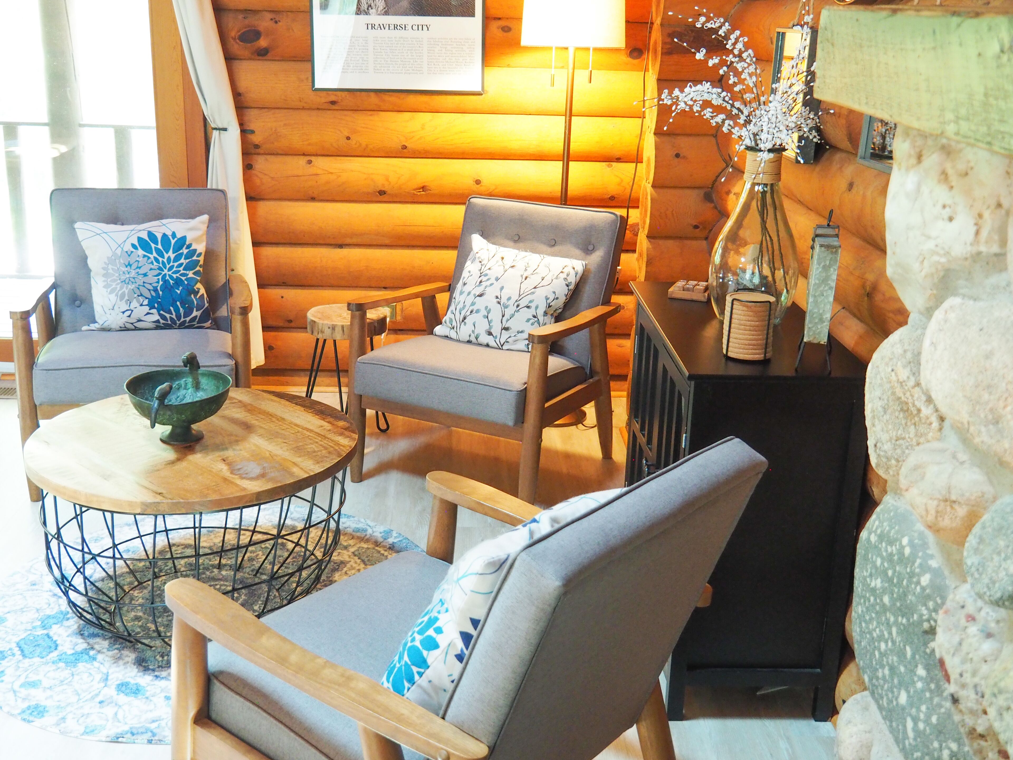 L’intérieur d’un chalet confortable, avec des murs en bois, une table à manger en bois, deux chaises rembourrées, un petit tabouret et un vase décoratif.