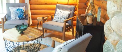 L’intérieur d’un chalet confortable, avec des murs en bois, une table à manger en bois, deux chaises rembourrées, un petit tabouret et un vase décoratif.