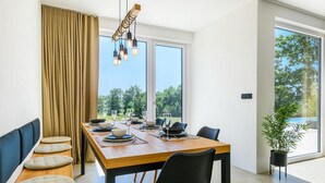 A modern dining area with a wooden table set for four, large windows offering a view of greenery, and a hanging light fixture. - 3 bedroom beautiful home in Porec (Porec)