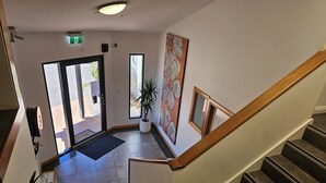 A hotel lobby with a staircase, a reception desk, a potted plant, and a large abstract painting.