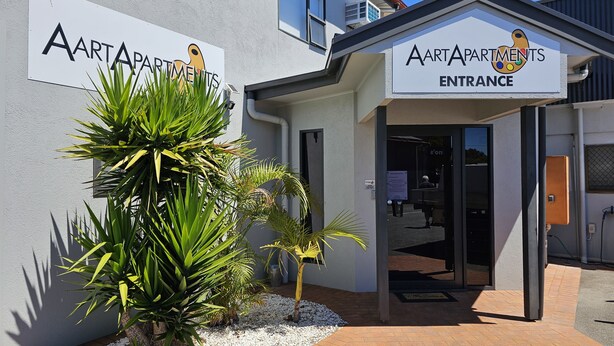 An AARTAPARTMENTS entrance with a sign, a door, and a small garden area with plants and pebbles.
