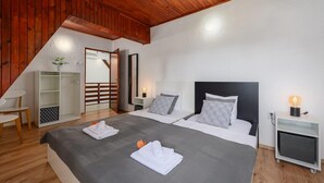 A bedroom with two beds, wooden ceiling, white walls, and a small bedside table with a lamp.