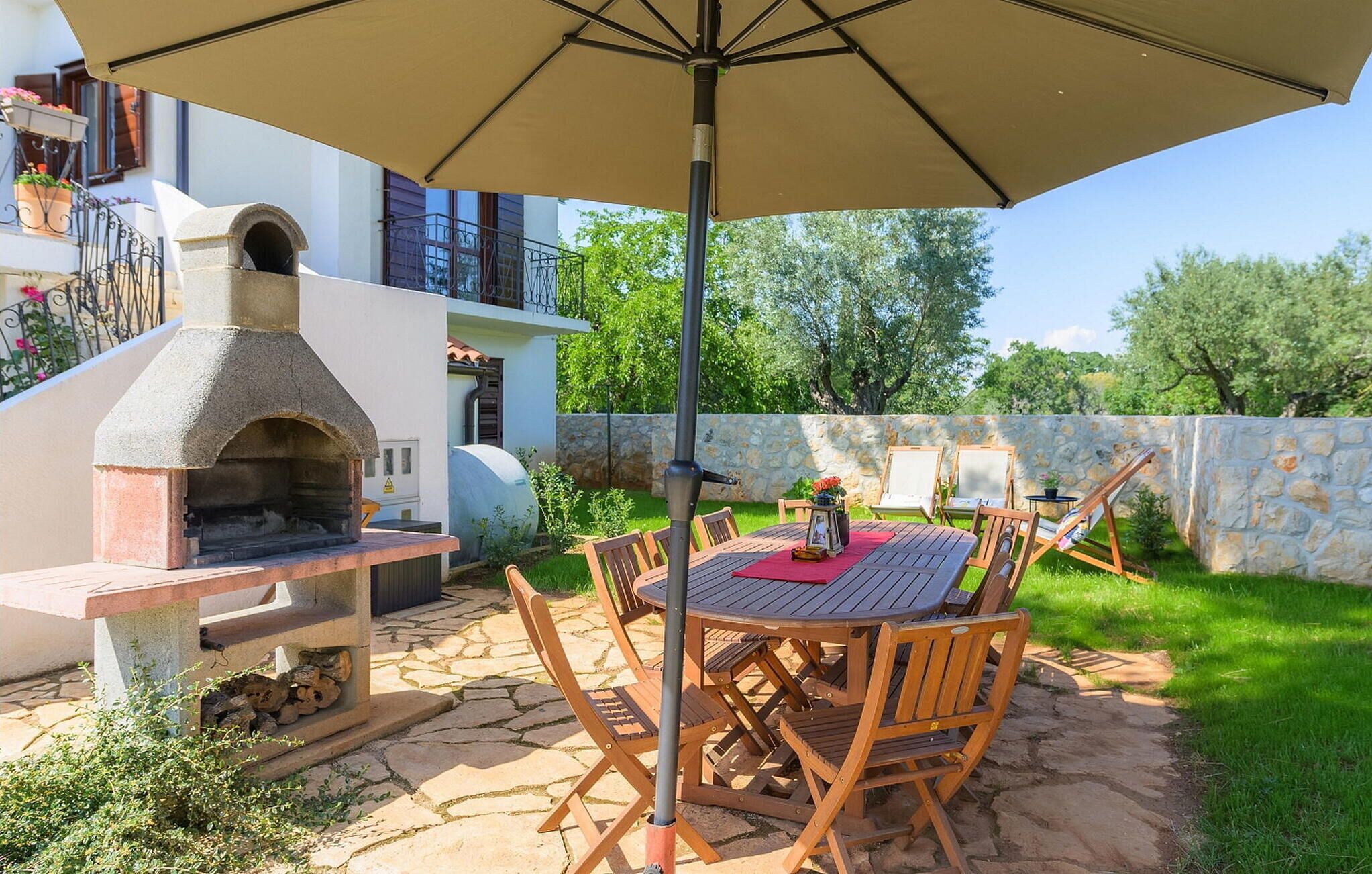 An outdoor patio with a stone oven, wooden chairs, and a table under a large umbrella.