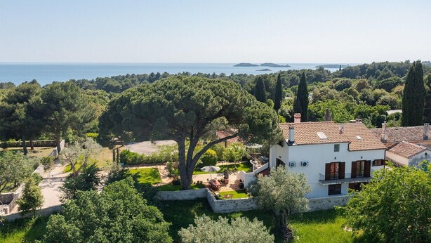 A villa with a garden, a view of the sea, and a mountainous backdrop.