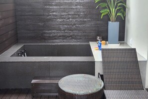 A modern bathroom with a bathtub, a wicker chair, a small round table, and a potted plant. - Hotel Noblion (Pohang)