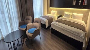 A hotel room with a bed, two chairs, a small table, and a bedside table with a lamp. - Hotel Noblion (Pohang)