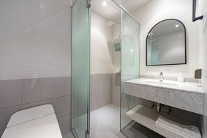 Un baño moderno con cabina de ducha de vidrio, un lavabo blanco sobre encimera de mármol y un espejo grande encima.