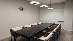 Un salón de conferencias con una larga mesa, seis sillas, tres lámparas colgantes y una pizarra en la pared.