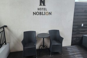 Letrero de hotel con dos sillones de mimbre y una mesa redonda pequeña en una terraza de madera.